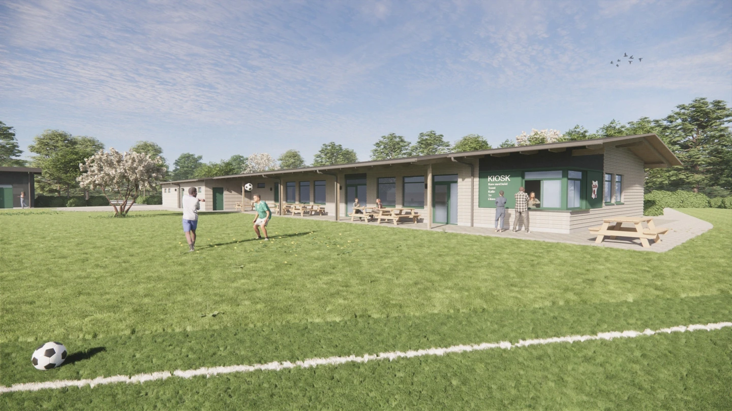 Fotbollsplan med barn som leker med boll, i bakgrunden syns en enplans byggnad med bänkar utanför och en litet kiosk